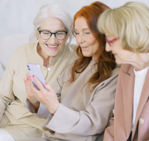 Three older women sitting together video calling using a smart phone